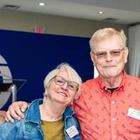 Man and woman standing together smiling for camera, with blue backdrop in background